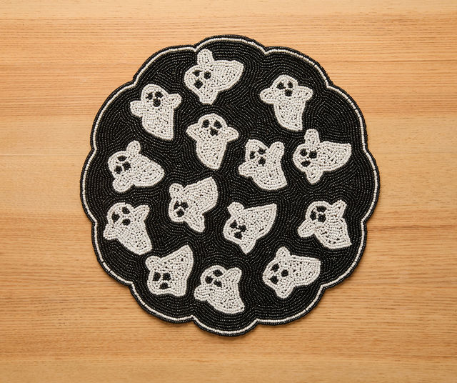 Round handmade beaded placemat featuring multiple cute white ghost patterns on a black background with a scalloped edge, designed as Halloween table decor.