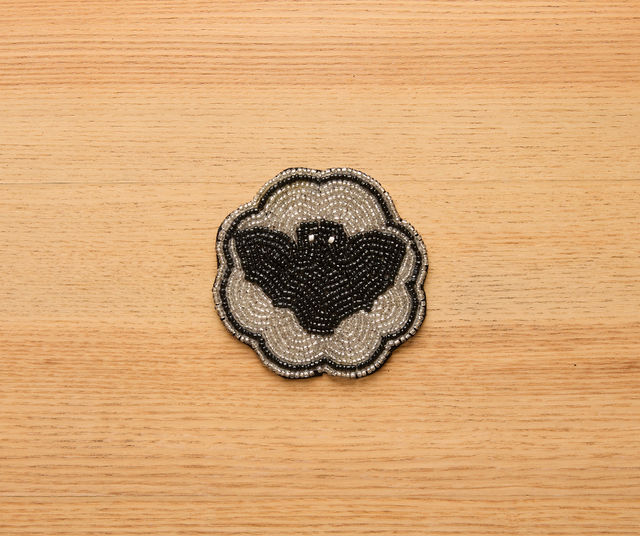 Handmade Halloween coaster with beaded black bat design on silver background and scalloped edge. Velvet backing. Ideal for spooky fall table decor.
