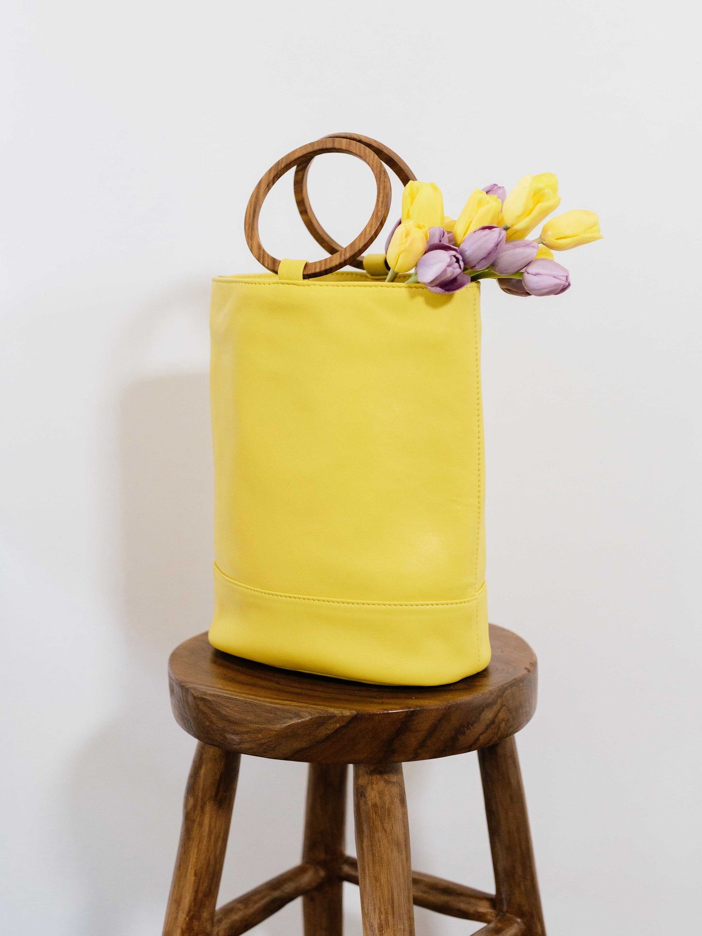 Leather Tote handbag on table with flowers sticking out -wood bucket tote lemon yellow color by payton james