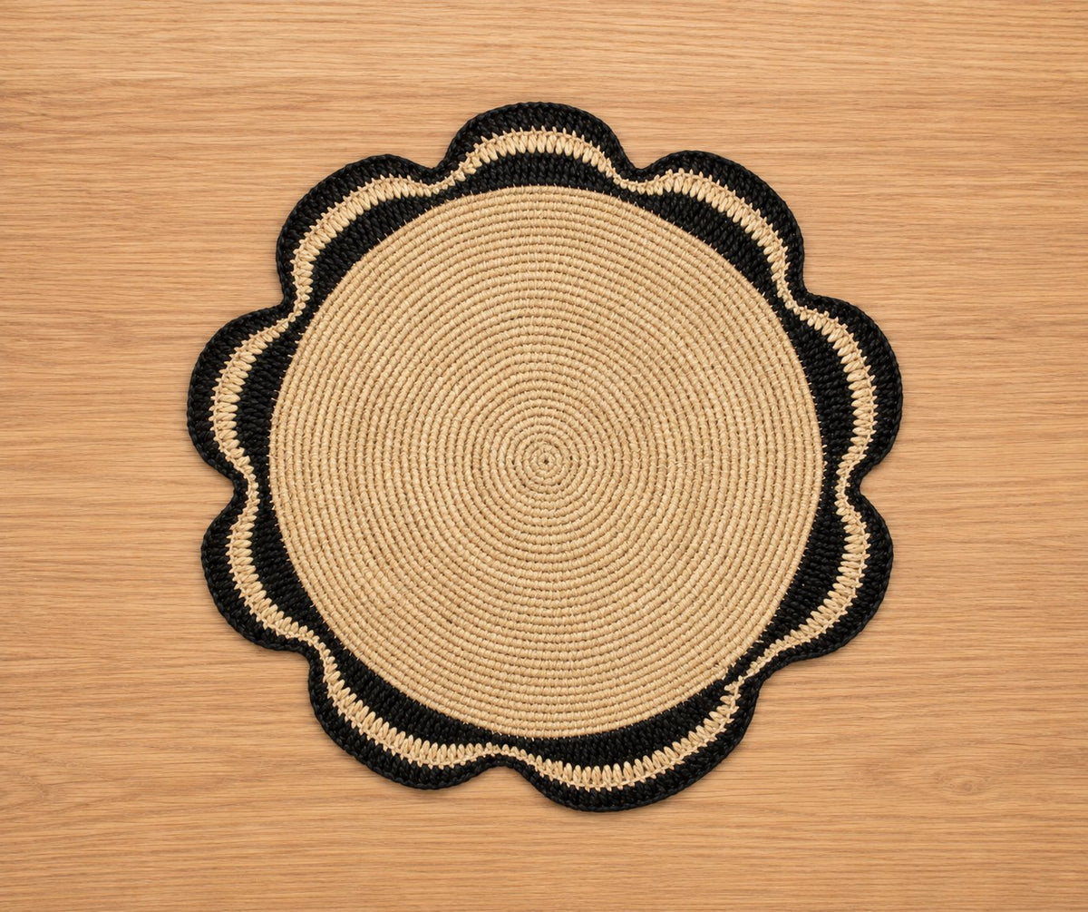 Black and natural scalloped raffia placemat on a light wood table