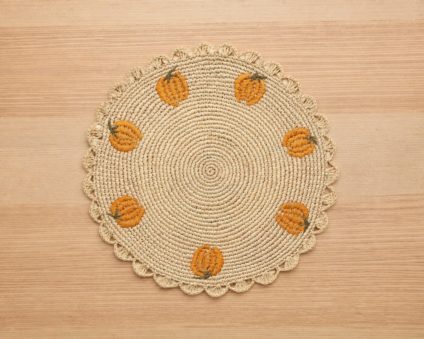 Handwoven raffia placemat with embroidered pumpkins on a light wood table