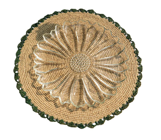 Round woven placemat with a glass plate on top, placed on a white fabric surface.